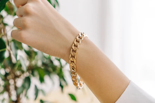 Golden bijouterie bracelet on woman hand. Plant.
